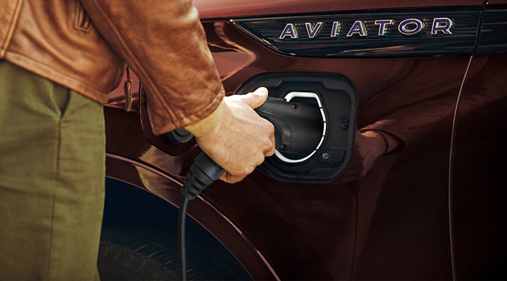 A hand is shown plugging a charger into the charging port of a 2023 Lincoln Aviator® Plug-in Hybrid model. | Purchase Lincoln in Mayfield KY