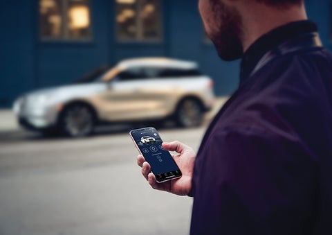 A person is shown interacting with a smartphone to connect to a Lincoln vehicle across the street. | Purchase Lincoln in Mayfield KY